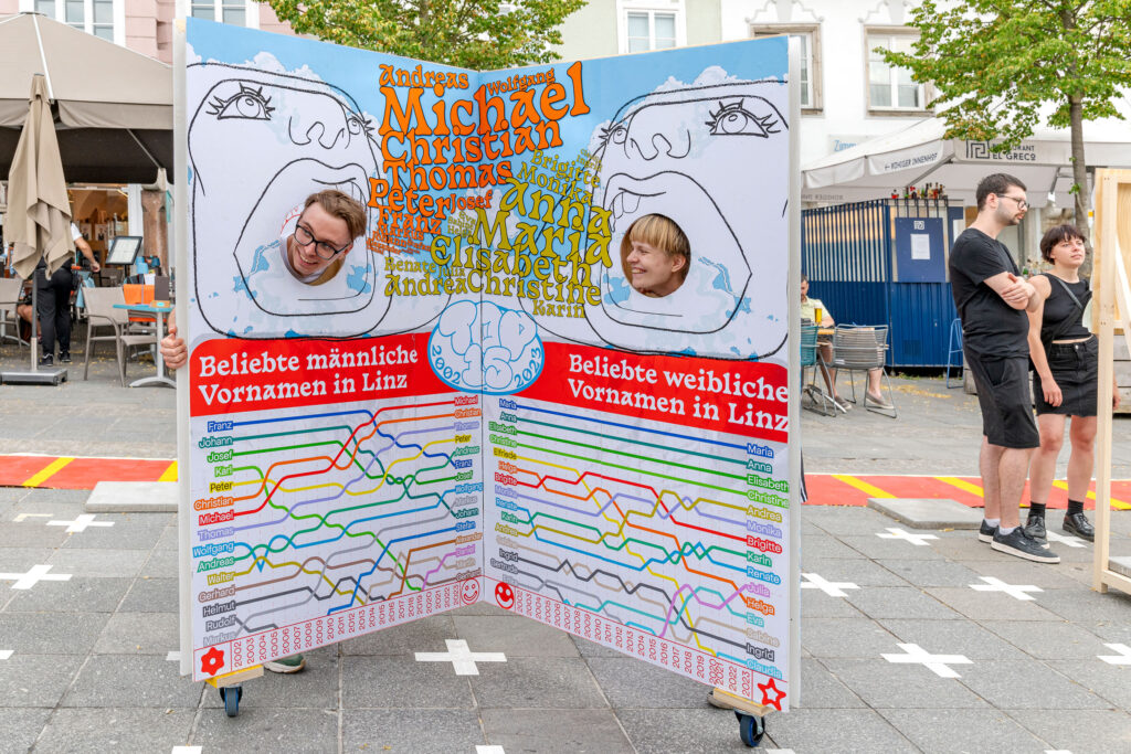 2 students pose with an exhibit on student names. 