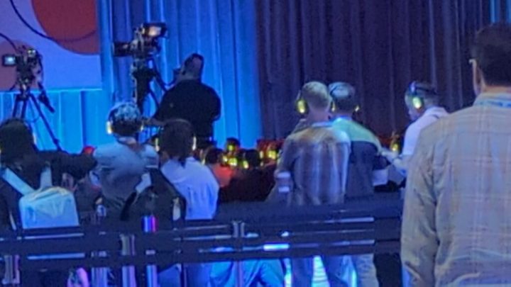 A zoomed-in and somewhat fuzzy photo depicting several people facing forward watching a presentation while wearing green glowing headphones.