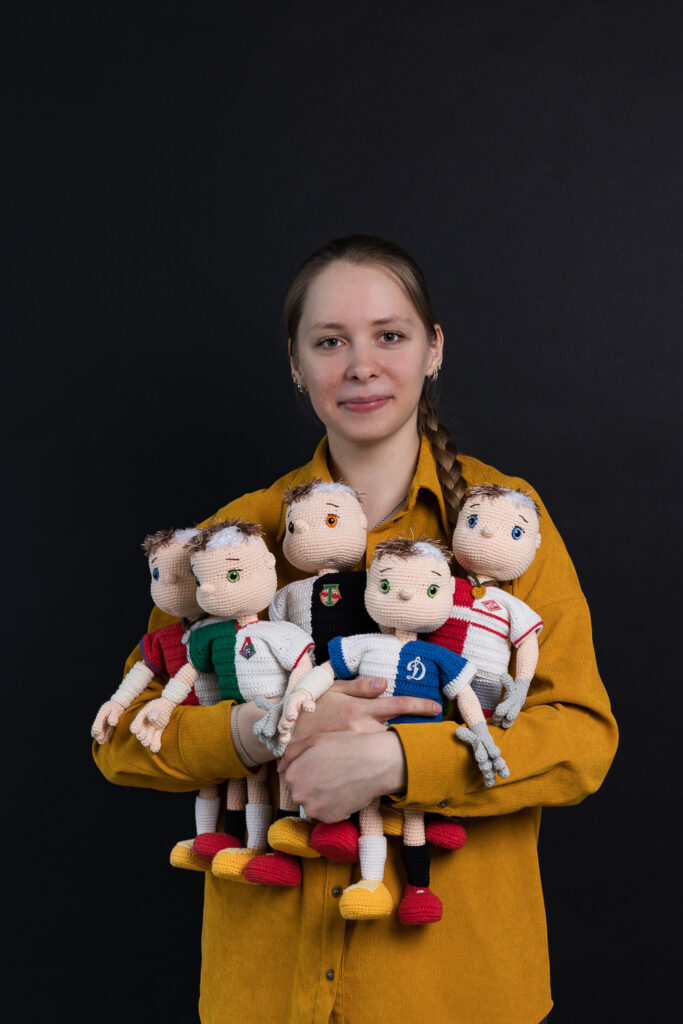 The author of the article, holding a series of crocheted football players, in various uniforms representing personalized statistics.
