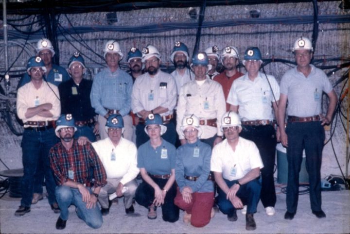 One of the teams consulting for the WIPP, underground wearing headlamps, smiling.