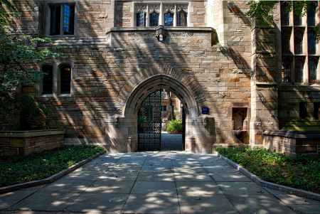 An old, brown brick building on a college campus with a steel gate that is half opened.