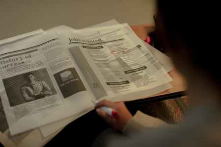 An over-the-shoulder view of a woman reviewing newspaper job advertisements.