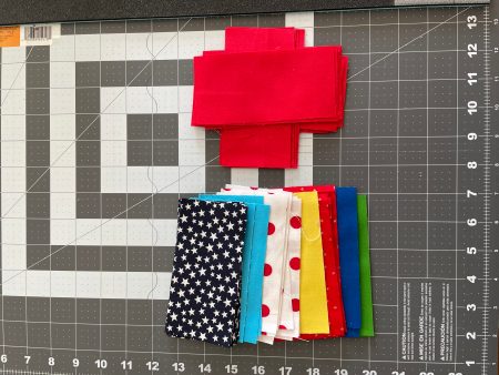 Assorted color fabric strips on a sewing table with grid and ruler.