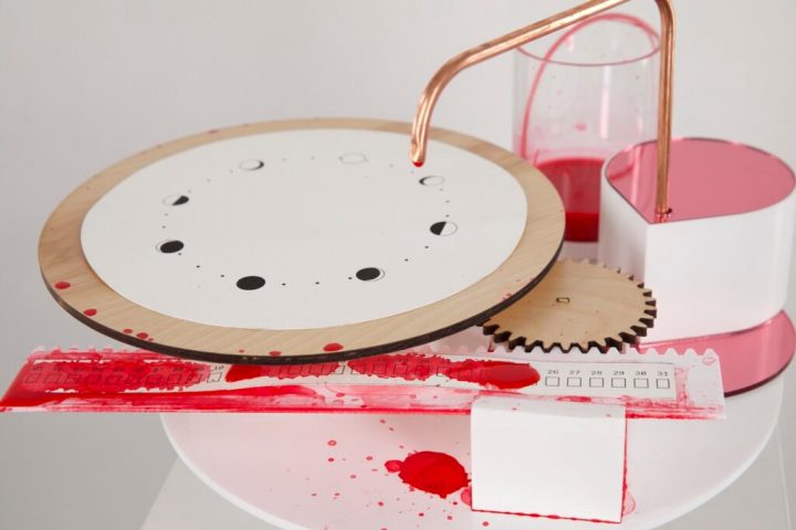 A photo of the setup, including a valve dripping red ink onto a strip of paper marked with 31 days. The paper moves on a gear system, and resets its position every 31 days.