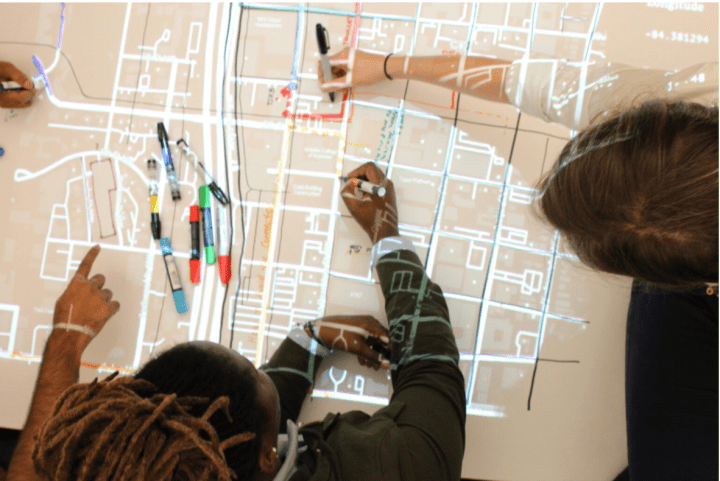 Exhibit participants use different colored markers to trace map lines projected onto large sheets of paper.