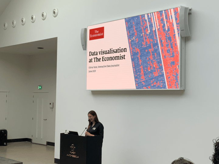 A photo of Olivia Vane at the lectern. The screen behind her says "Data Visualization at the Economist"