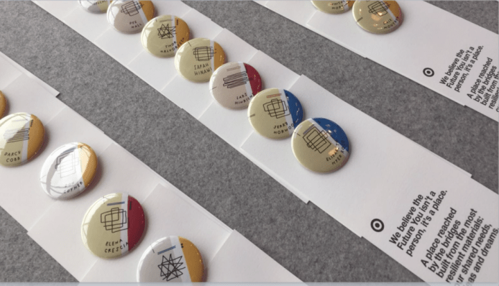 Pins laid out with a card which reads, "we believe the future you isn't a person, it's a place. A place reached by the bridges built from the most resilient materials: our shared needs and dreams.