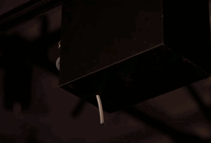 A black box, suspended from a belt-pully system drips calligraphy ink.